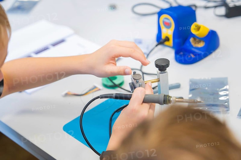 Person soldering electronic components on a workbench with a soldering iron, Youth Research Centre