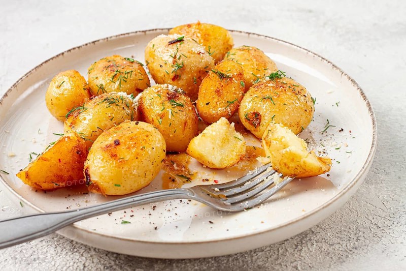 Half-eaten fried new potatoes, with butter and dill, on a white plate, with a fork, at home, no people