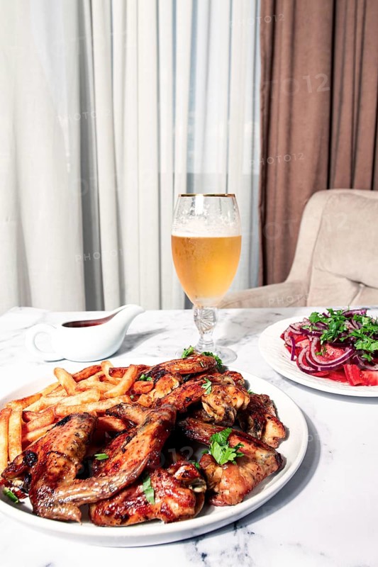 Delicious barbecue chicken wings, with French fries, salad and a refreshing drink, at a cozy table, there are no people