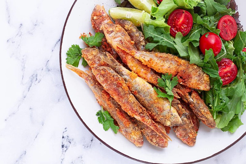 Fried crispy mullet fish, with fresh salad, on a plate with lime, no people