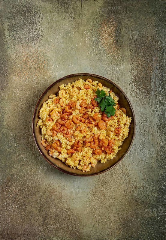 Risotto with shrimp, in a bowl, on a textured surface, with a side dish of fresh coriander, homemade, no people