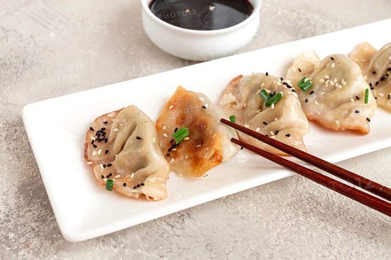 Gyoza Japanese dumplings, fried, with sauce, green onion, and sesame seeds, natural color, light background
