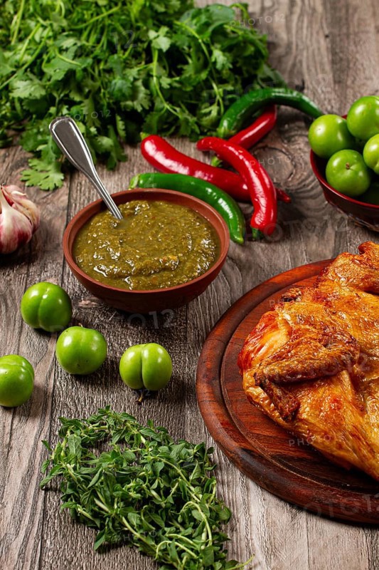 Baked tobacco chicken, served with tkemali sauce, on a wooden table, Georgian cuisine, rustic style, no people