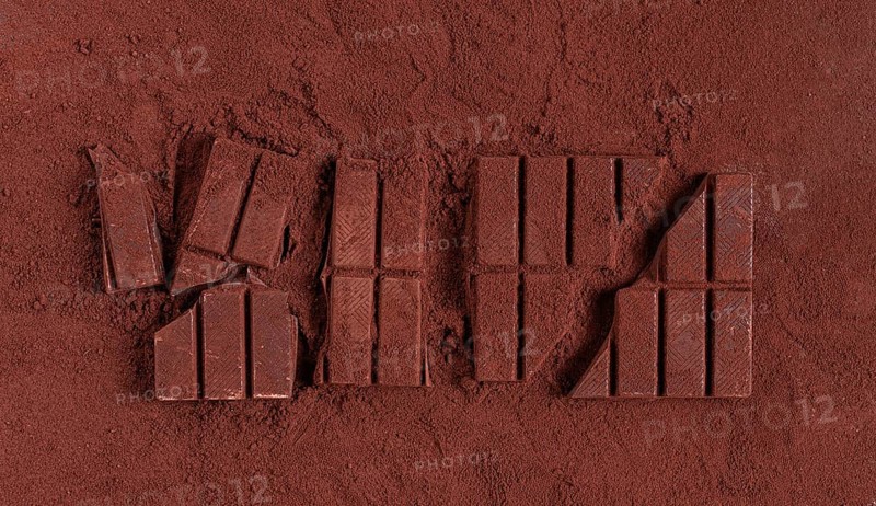 Chocolate bars broken and scattered on cocoa powder background with rich texture and color