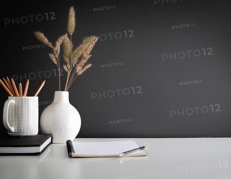 A clean and modern office workspace featuring a pen holder, notebook, and ceramic vase against a dark wall, AI generated
