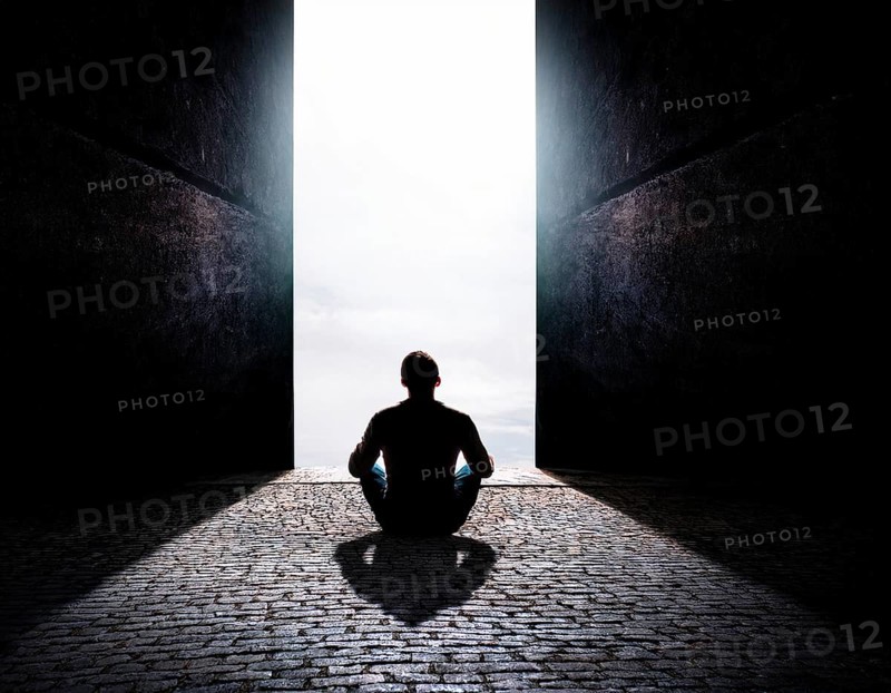Silhouette of a person sitting alone within a brick archway, observing a peaceful and scenic cloudy horizon, evoking feelings of solitude, introspection, and calmness, AI generated