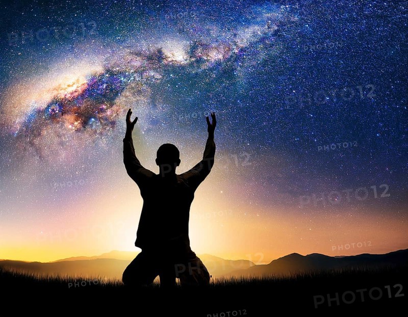 A man kneels in peaceful reflection under the vibrant Milky Way galaxy at sunset in an open natural setting, making prays, AI generated