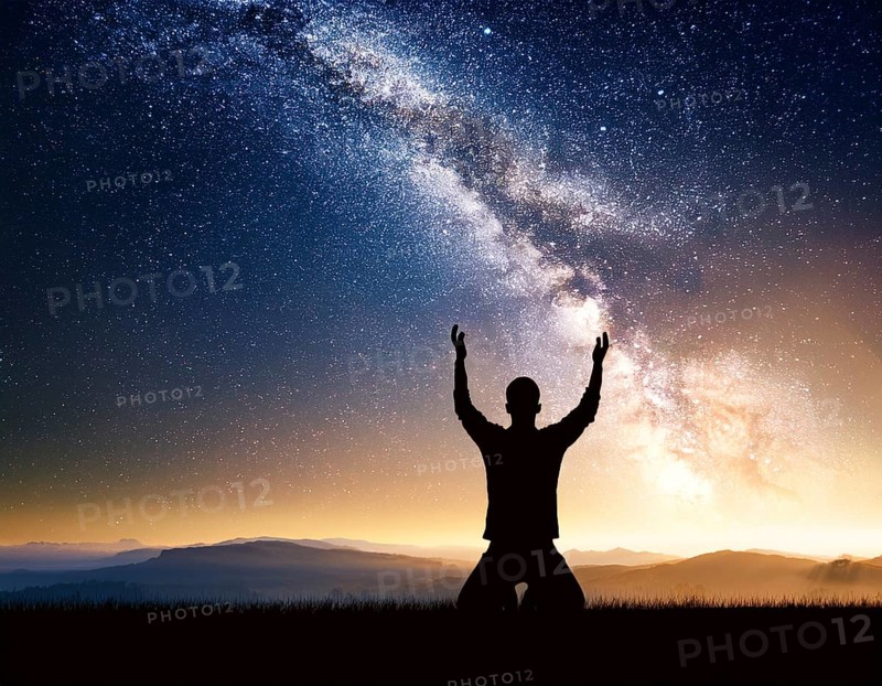 A man kneels in peaceful reflection under the vibrant Milky Way galaxy at sunset in an open natural setting, making prays, AI generated