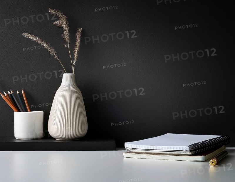 A clean and modern office workspace featuring a pen holder, notebook, and ceramic vase against a dark wall, AI generated