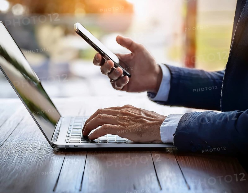A man in a professional office environment multitasking with a smartphone and laptop, conveying productivity, technology integration, and modern working practices, AI generated