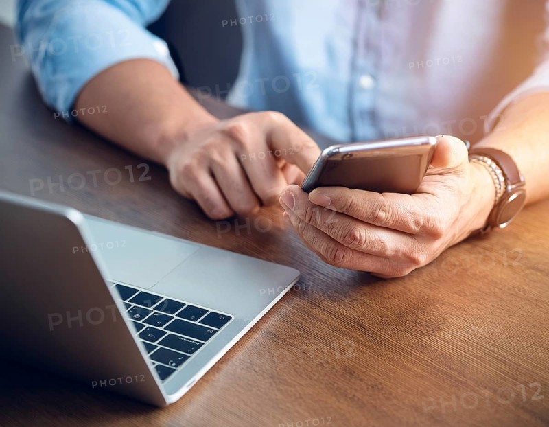 A man in a professional office environment multitasking with a smartphone and laptop, conveying productivity, technology integration, and modern working practices, AI generated