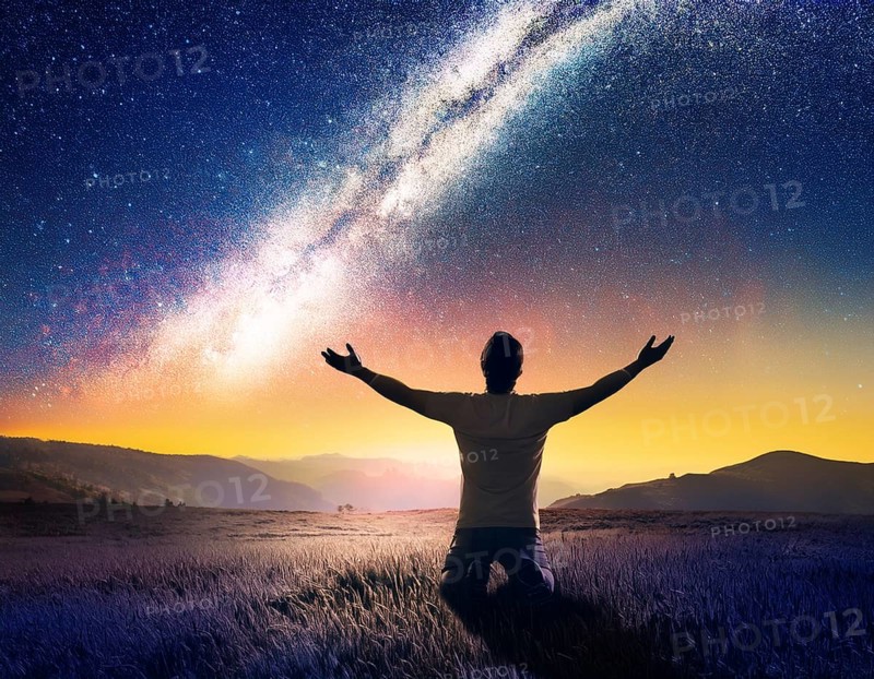 A man kneels in peaceful reflection under the vibrant Milky Way galaxy at sunset in an open natural setting, making prays, AI generated