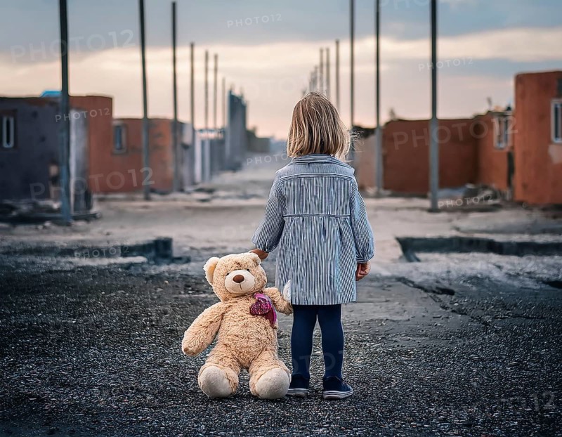 A young child stands alone holding a teddy bear in an urban outdoor setting, symbolizing innocence and isolation, AI generated