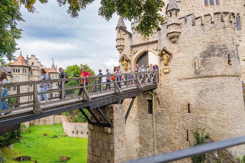 Group of tourists crossing a historic wooden bridge at a majestic castle gate, Lichtenstein Castle, Lichtenstein, Swabian Alb, Germany