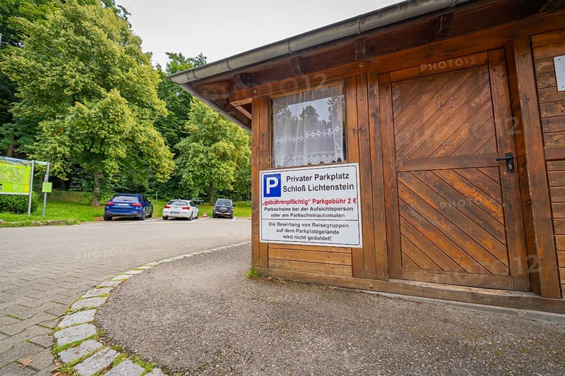A small car park with a wooden hut and parked cars at the edge of the forest, Lichtenstein Castle, Lichtenstein, Swabian Alb, Germany