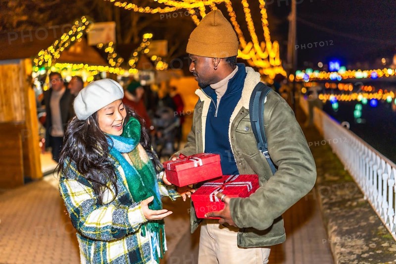Happy multiethnic couple exchanging christmas gifts at a christmas market, enjoying winter holidays and christmas spirit
