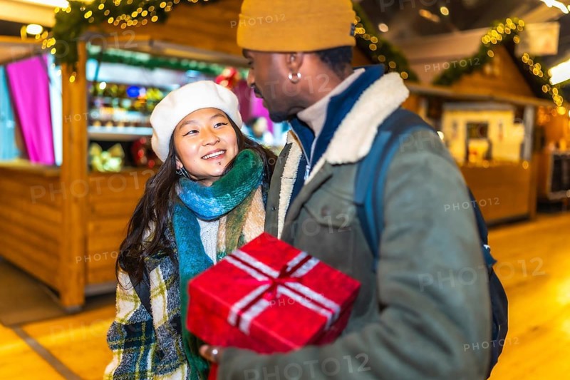 Young multiethnic couple holding a christmas gift, enjoying christmastime at a christmas market