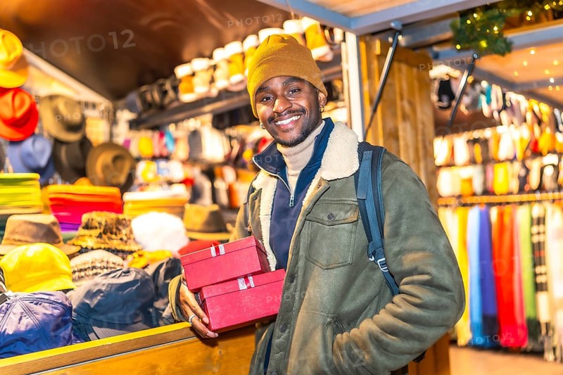 Young man holding christmas presents at a christmas market stall, enjoying the festive atmosphere