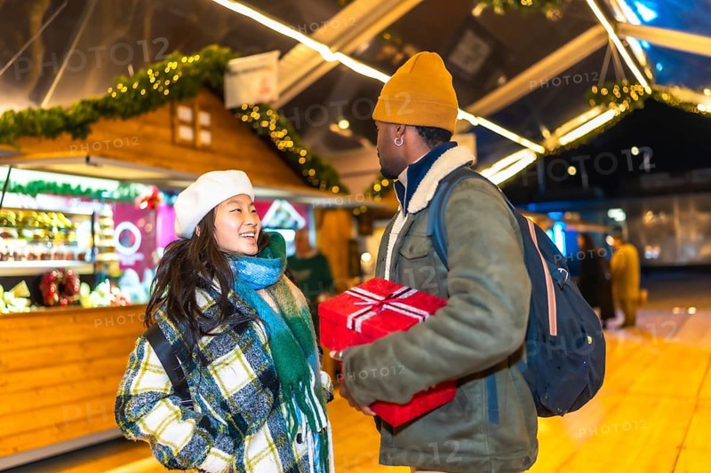 Young multiethnic couple exchanging christmas gifts at a christmas market, enjoying the festive atmosphere and holiday spirit