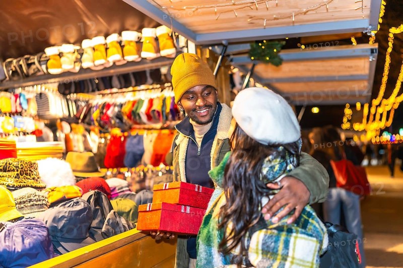 Happy multiethnic couple exchanging christmas presents at a stall in a christmas market at night