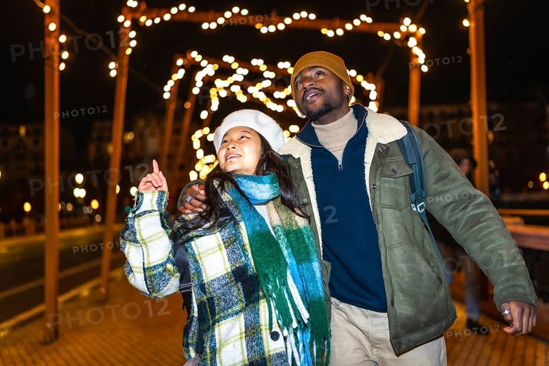Young multiethnic couple walking hand in hand, admiring the enchanting christmas lights and festive decorations on a winter night
