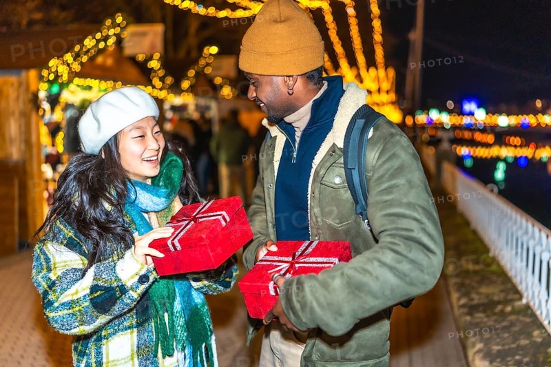 Young multiethnic couple exchanging christmas gifts at a christmas market, enjoying the festive atmosphere