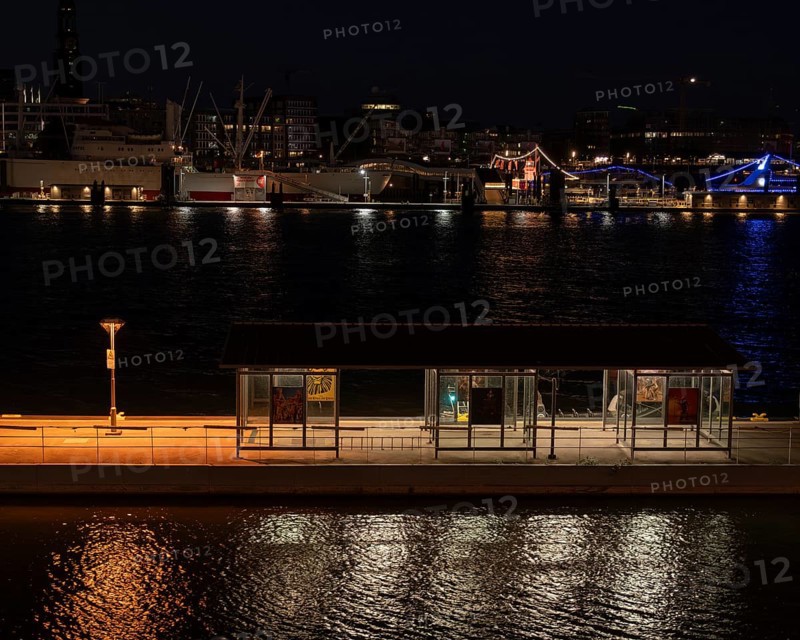 Night shot of a pontoon with bus shelter at the theatre on the Elbe with a view of the lighting of the Landungsbrücken, Hamburg, Germany