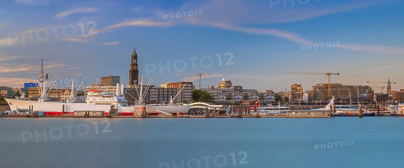 View over the Norderelbe to the main church St. Michaelis and the Landungsbrücken with ships in front of it in the evening light, long exposure, Hamburg, Germany