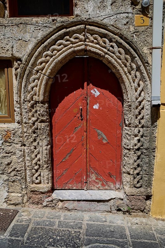 Red door with Romanesque arch and decorative stone carvings in an old façade, Turkish Quarter, Rhodes Old Town, Rhodes Town, Rhodes, Dodecanese, Greek Islands, Greece