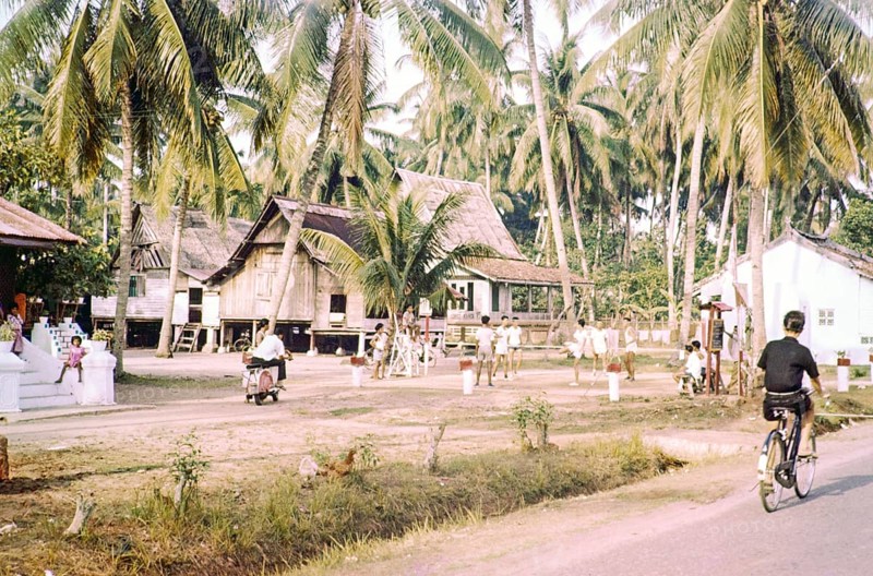 Traditional village houses in coconut palm trees, boys and young men playing Sepak Takraw foot volleyball game, Malacca or Melaka, Malaya, Malaysia, south east Asia c 1964