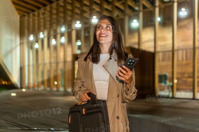 Young businesswoman walking confidently at night in an urban setting, carrying a briefcase and using a smartphone, embodying determination and modern communication in her professional journey