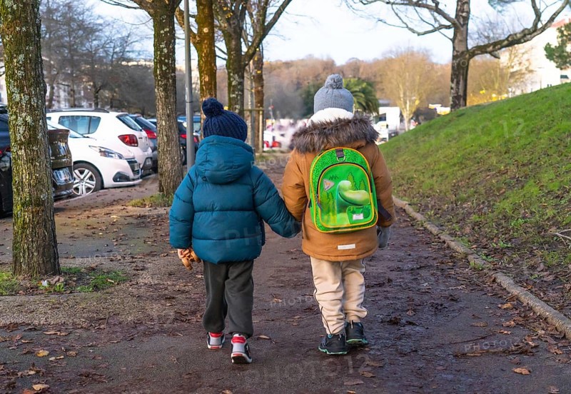 Two young children holding hands and walking home from school on a chilly winter day in bayonne, france