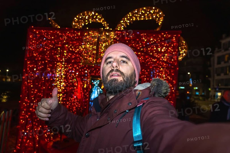 Tourist taking a selfie and making thumbs up sign with christmas lights and decorations in bayonne, france