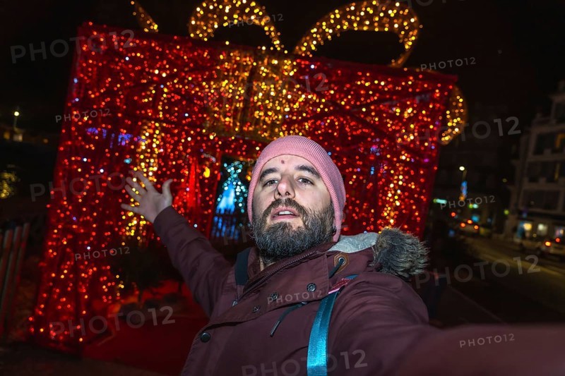 Bearded man taking a selfie in front of giant luminous christmas gift box in bayonne, france