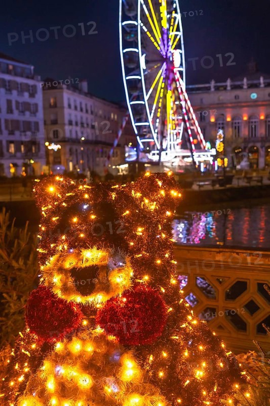 Luminous christmas bear decoration shining brightly in bayonne, france, with a ferris wheel and festive lights illuminating the background at night