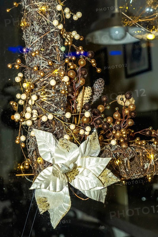 Festive christmas wreath adorned with golden and white poinsettia, berries, and string lights brightens a bayonne window