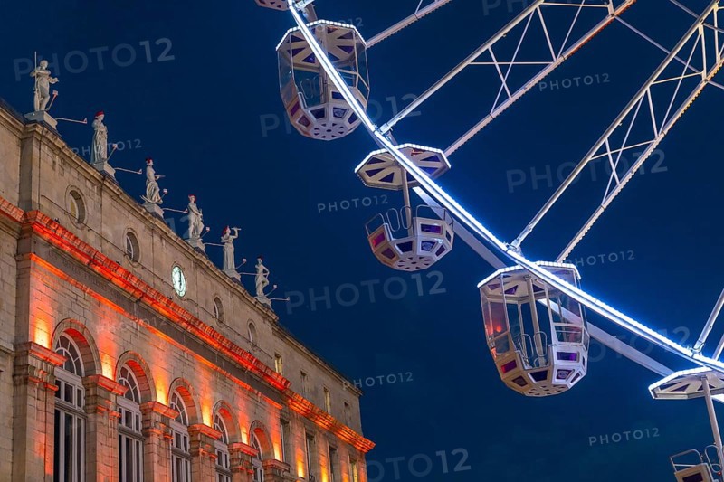 Ferris wheel cabins rotating over bayonne city hall illuminated in orange during christmas night in france