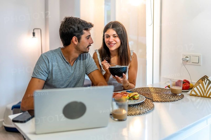 Young couple sharing a delightful breakfast while working remotely, enjoying each other's company and embracing modern life at home