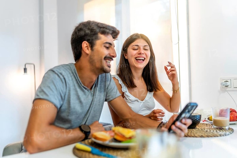 Young couple enjoying breakfast and having fun while using a smartphone in their modern kitchen