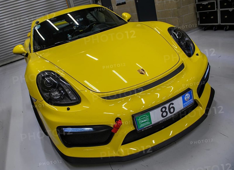Dynamic photo front of sports car racing car yellow Porsche Cayman GT4 with front left mounted red tow strap, international