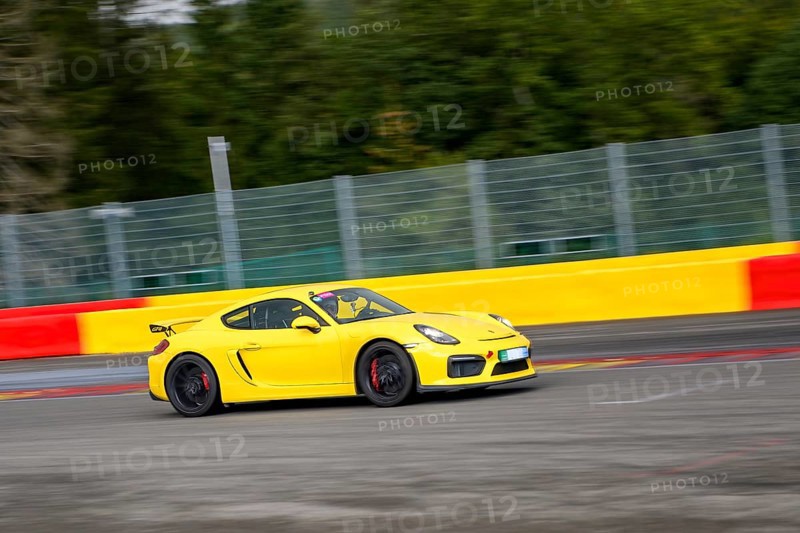 Yellow racing car sports car Porsche Cayman GT4 races at high speed top speed during trackday on FIA Formula 1 race track, Circuit de Spa Francorchamps, Ardennes rollercoaster, Ardennes, Malmedy, Belgium