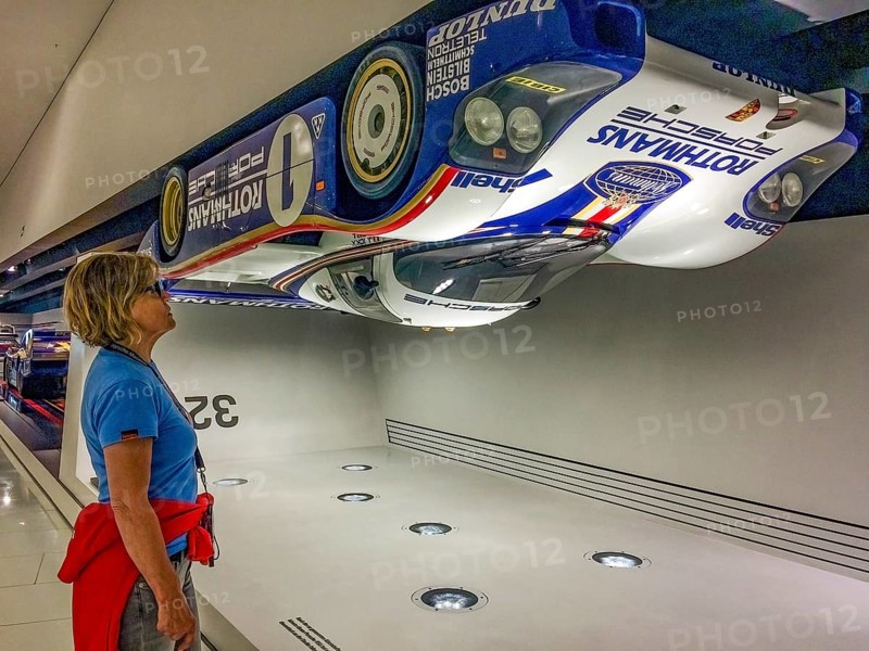 Visitor to the museum looks upwards at a Porsche 956 racing car hanging upside down under the ceiling of the museum as an example of high contact pressure at 321.4 kilometres per hour, Porsche Museum, Stuttgart, Baden-Württemberg, Germany