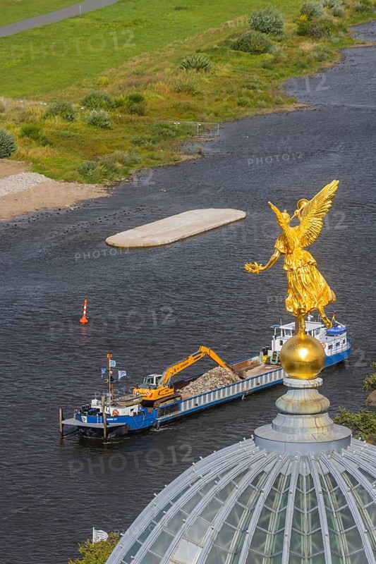 View from the lantern of the Church of Our Lady. Fama (the goddess of rumours) on the dome of the Academy of Fine Arts, with the pillar foundations of the former Carola bridges. The dredger Domarin straightens the fairway for shipping, Dresden, Saxony, Germany