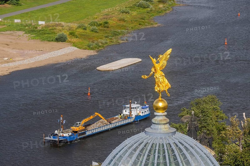 View from the lantern of the Church of Our Lady. Fama (the goddess of rumours) on the dome of the Academy of Fine Arts, with the pillar foundations of the former Carola bridges. The dredger Domarin straightens the fairway for shipping, Dresden, Saxony, Germany
