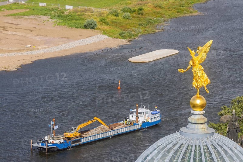 View from the lantern of the Church of Our Lady. Fama (the goddess of rumours) on the dome of the Academy of Fine Arts, with the pillar foundations of the former Carola bridges. The dredger Domarin straightens the fairway for shipping, Dresden, Saxony, Germany