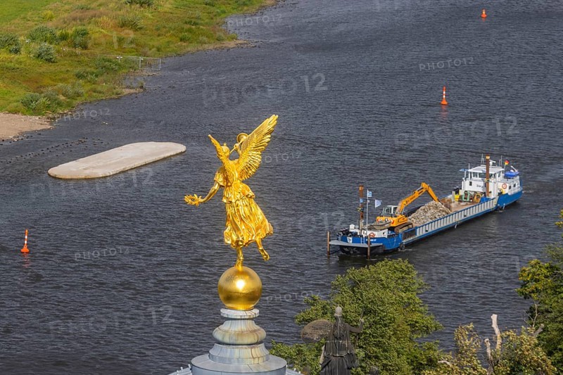 View from the lantern of the Church of Our Lady. Fama (the goddess of rumours) on the dome of the Academy of Fine Arts, with the pillar foundations of the former Carola bridges. The dredger Domarin straightens the fairway for shipping, Dresden, Saxony, Germany