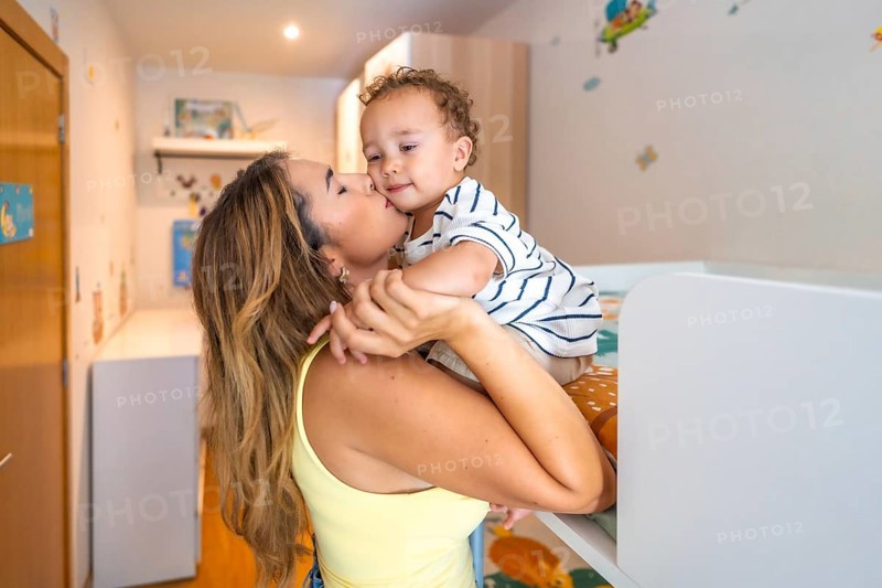 Mom kissing her baby boy in a decorated bedroom, showing love and affection in a cozy home environment