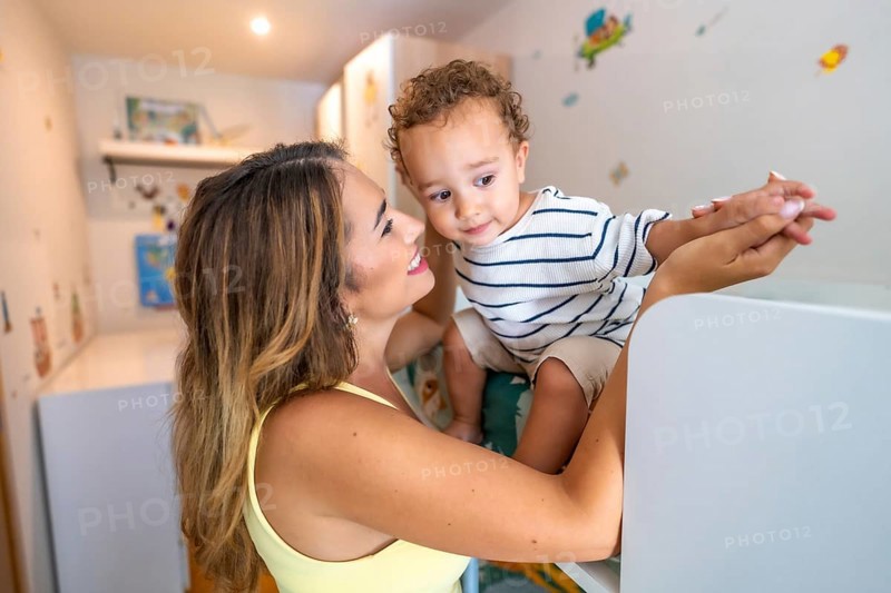 Smiling mother holding hands with her baby son while playing in a decorated children's bedroom