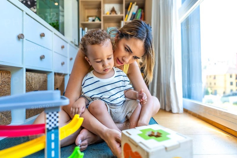 Mom and her son are sitting on the floor enjoying playtime with colorful educational toys, promoting early childhood development and quality time together