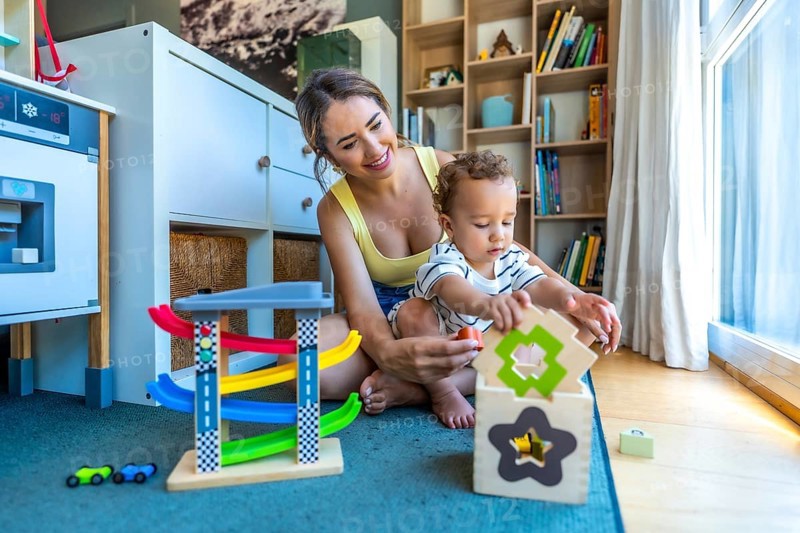 Happy mother and her cute son are playing together with colorful educational toys in a modern playroom